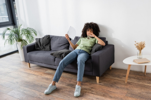 woman on the couch feeling warm using a hand fan depicting the cooling limitation of portable air conditioner