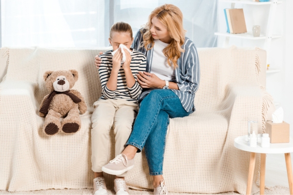 mom assisting sneezing daughter depicting physical symptoms of poor indoor air quality