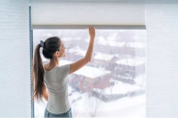 woman closing window blinds during winter