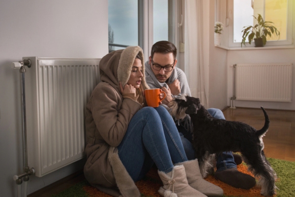 couple feeling cold sitting by the radiator with their dog due to malfunctioning heating system caused by frozen fuel oil